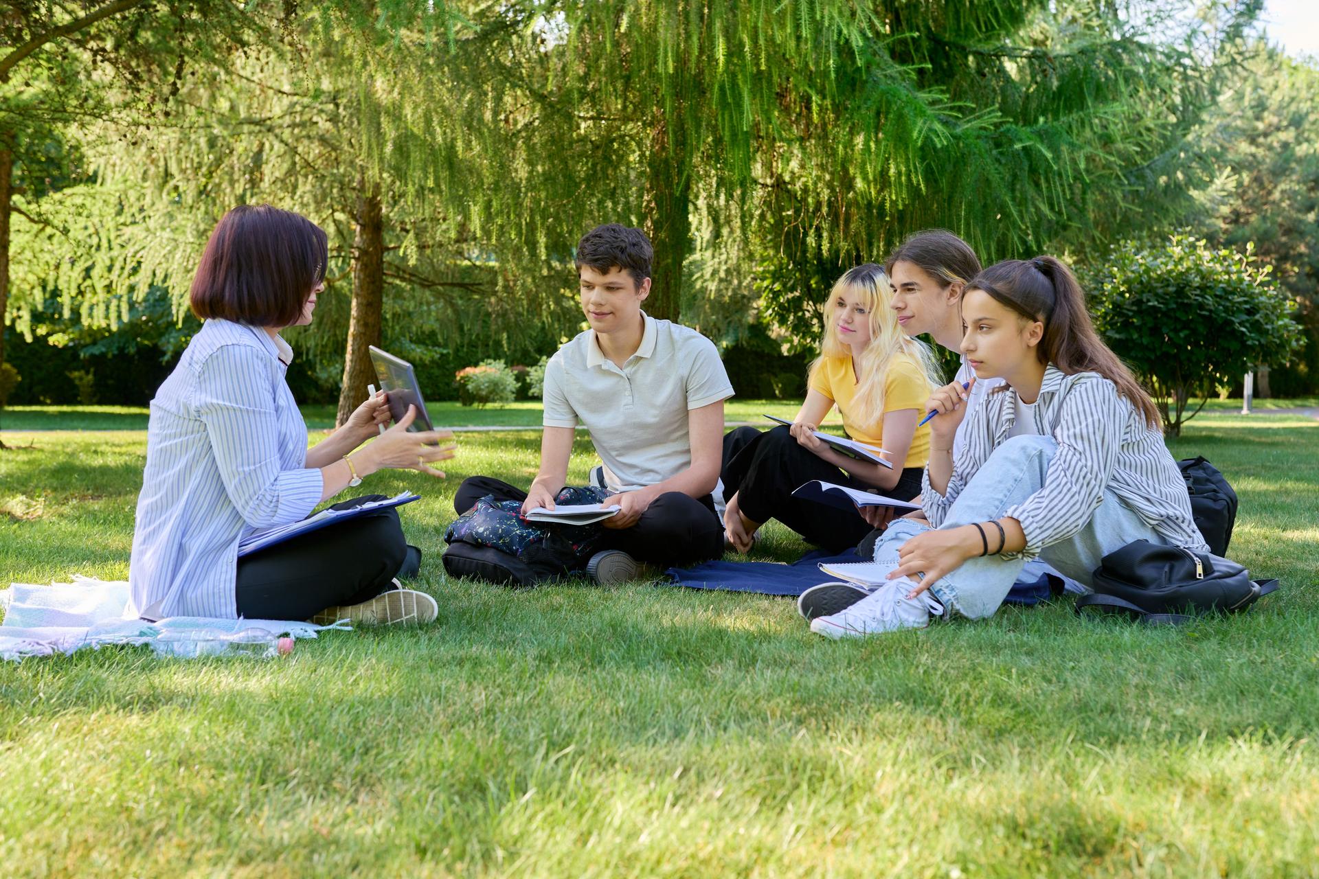 Outdoor, group of students with female teacher sitting on grass