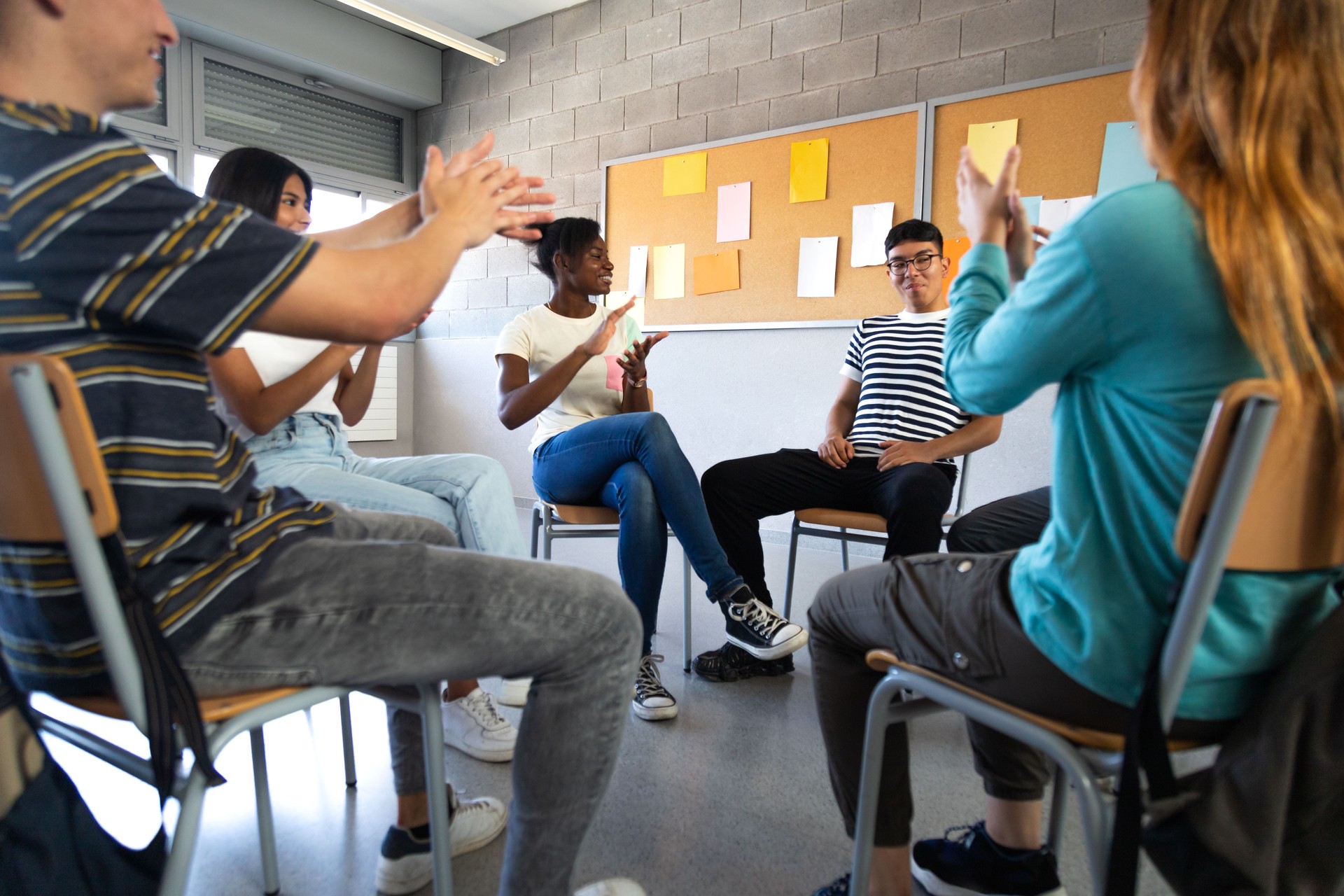 Teen student receives praise from classmates. Multiracial group of high school students sitting in a circle clapping.