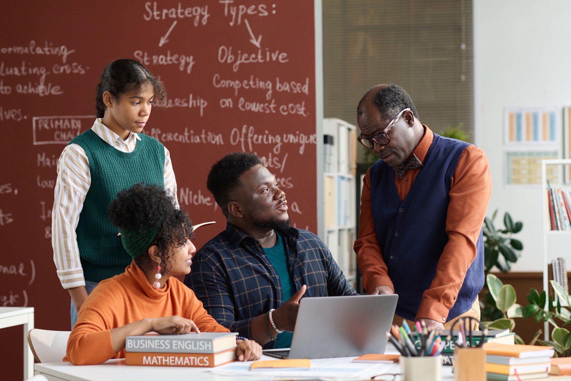 Senior Black Teacher Talking to Group of Students with Books and Computer